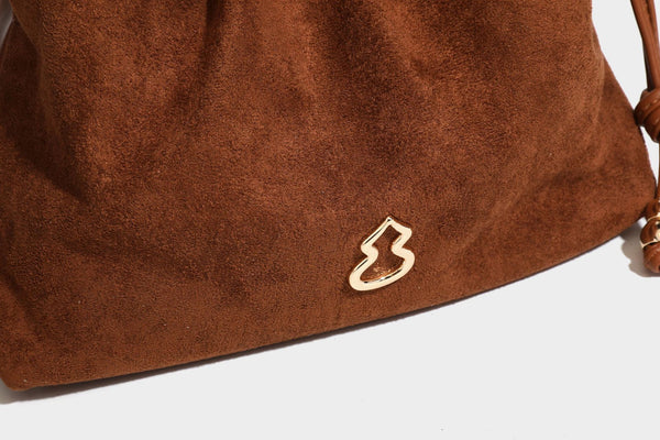Suede-look drawstring shoulder bag in brown with smooth trim, knotted bead drawstring closure, slim adjustable strap, and