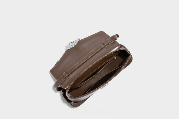Small structured saddle bag with glossy leather-look finish, angular flap front, silver-tone metal clasp, and slim