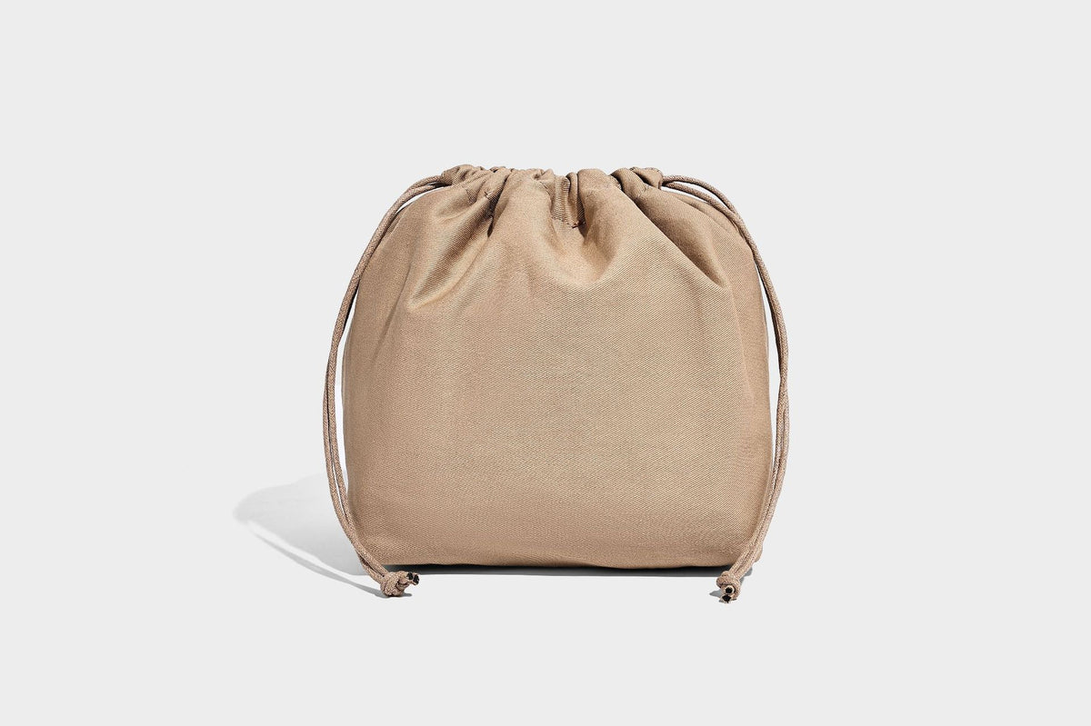 Woven straw-look tote bag in tan and cream with dark brown leather-look trim, long flat shoulder straps, and tassel bead