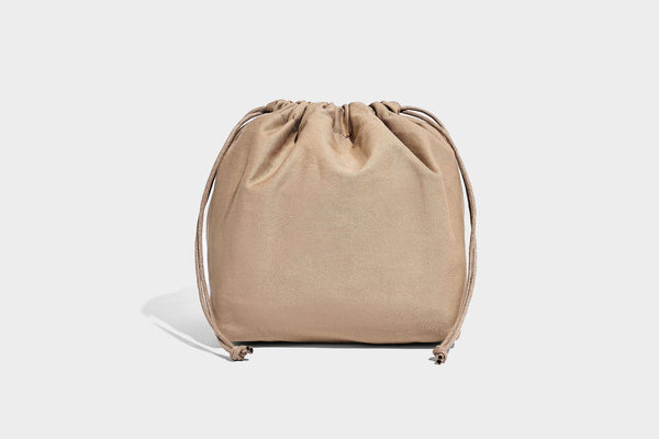 Woven straw-look tote bag in tan and cream with dark brown leather-look trim, long flat shoulder straps, and tassel bead