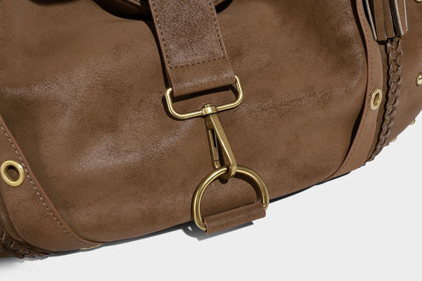 Slouchy crescent hobo bag in matte brown suede-like finish with gold-tone studs, grommets, braided top handle, tassel side