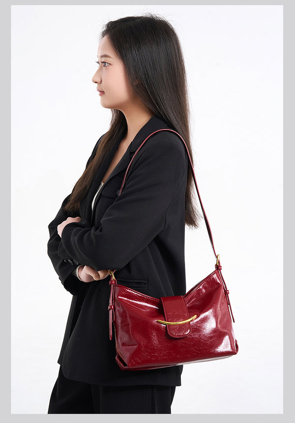 Glossy burgundy leather-look shoulder bag with curved gold-tone bar front closure, crinkled oil-wax texture, and adjustable