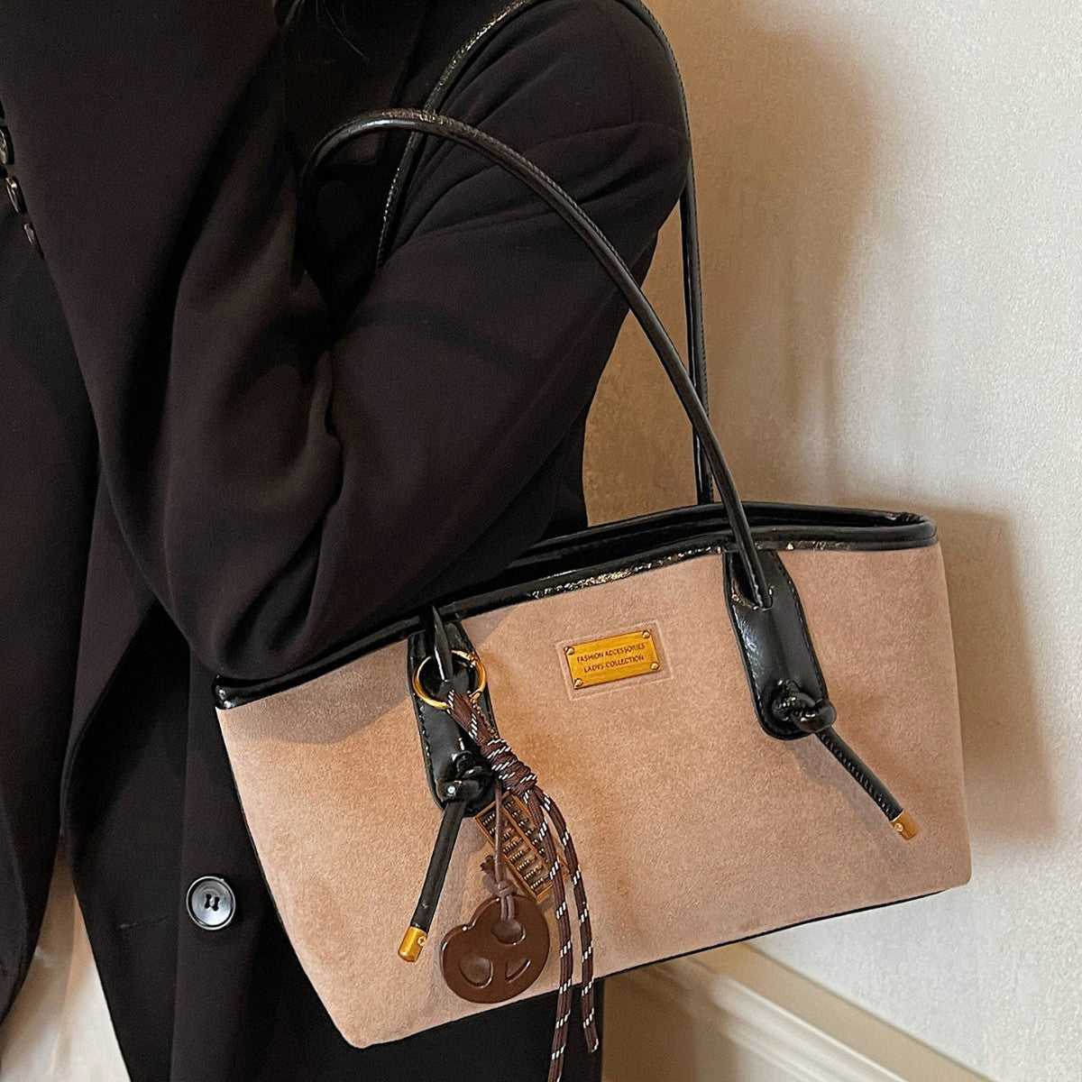 Structured suede-finish tote bag with glossy black leather-look trim, dual top handles, and decorative hanging charm in