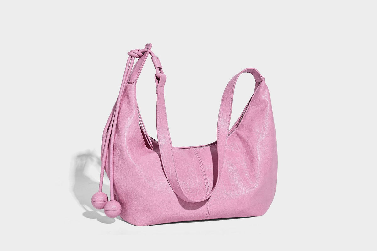 Slouchy crescent half-moon shoulder bag in pink pebbled textured finish with floral charm and knotted side detail, detail