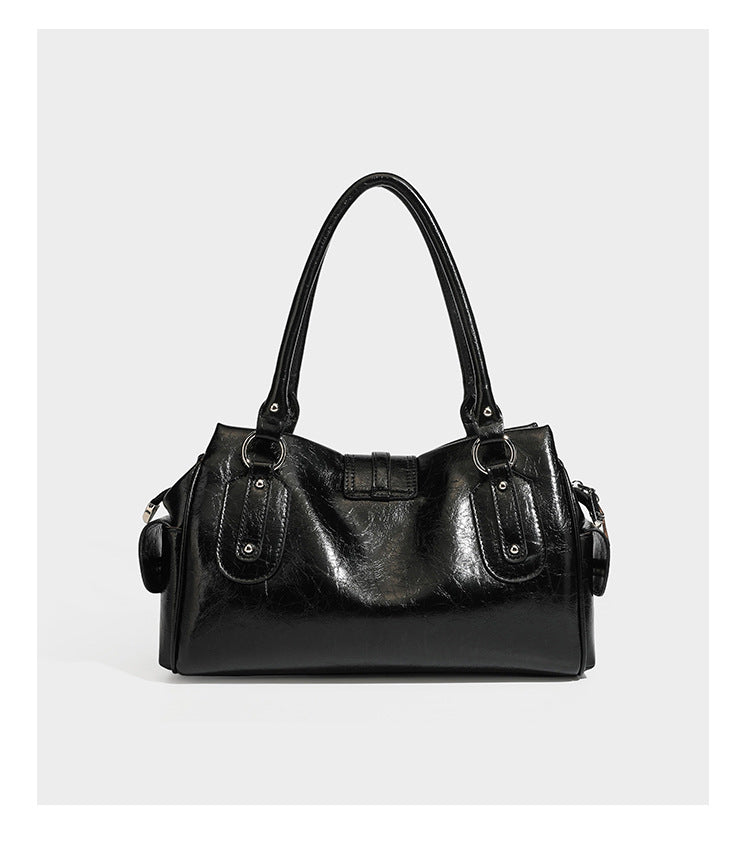 Glänzende, geknautschte Barrel-Satchel mit zwei oberen Tragegriffen, vorderem Klappen-Riemen-Panel, Ring- und Nietenbeschlägen sowie einem abnehmbaren