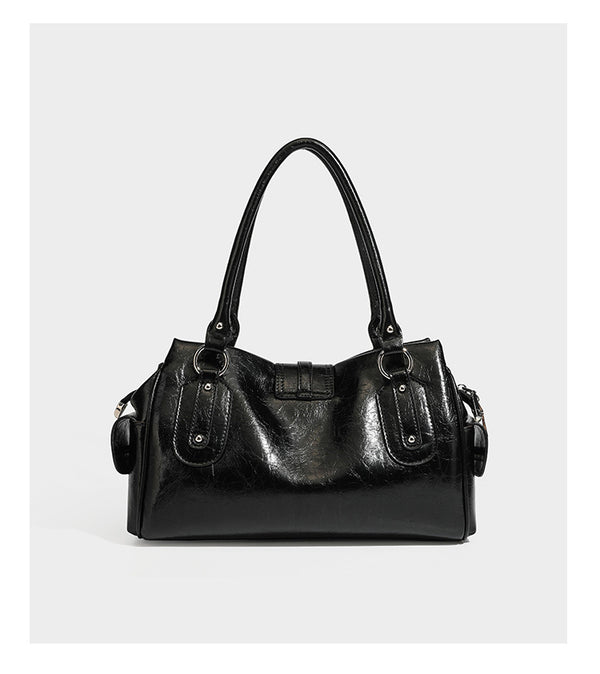 Glänzende, geknautschte Barrel-Satchel mit zwei oberen Tragegriffen, vorderem Klappen-Riemen-Panel, Ring- und Nietenbeschlägen sowie einem abnehmbaren