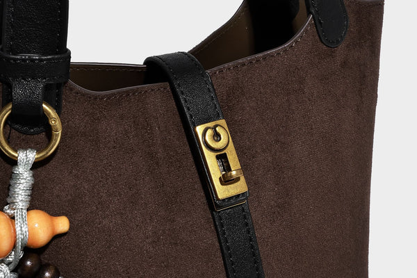 Small structured trapezoid tote bag in matte suede-look finish with black contrast trim, gold-tone front clasp, tassel charm