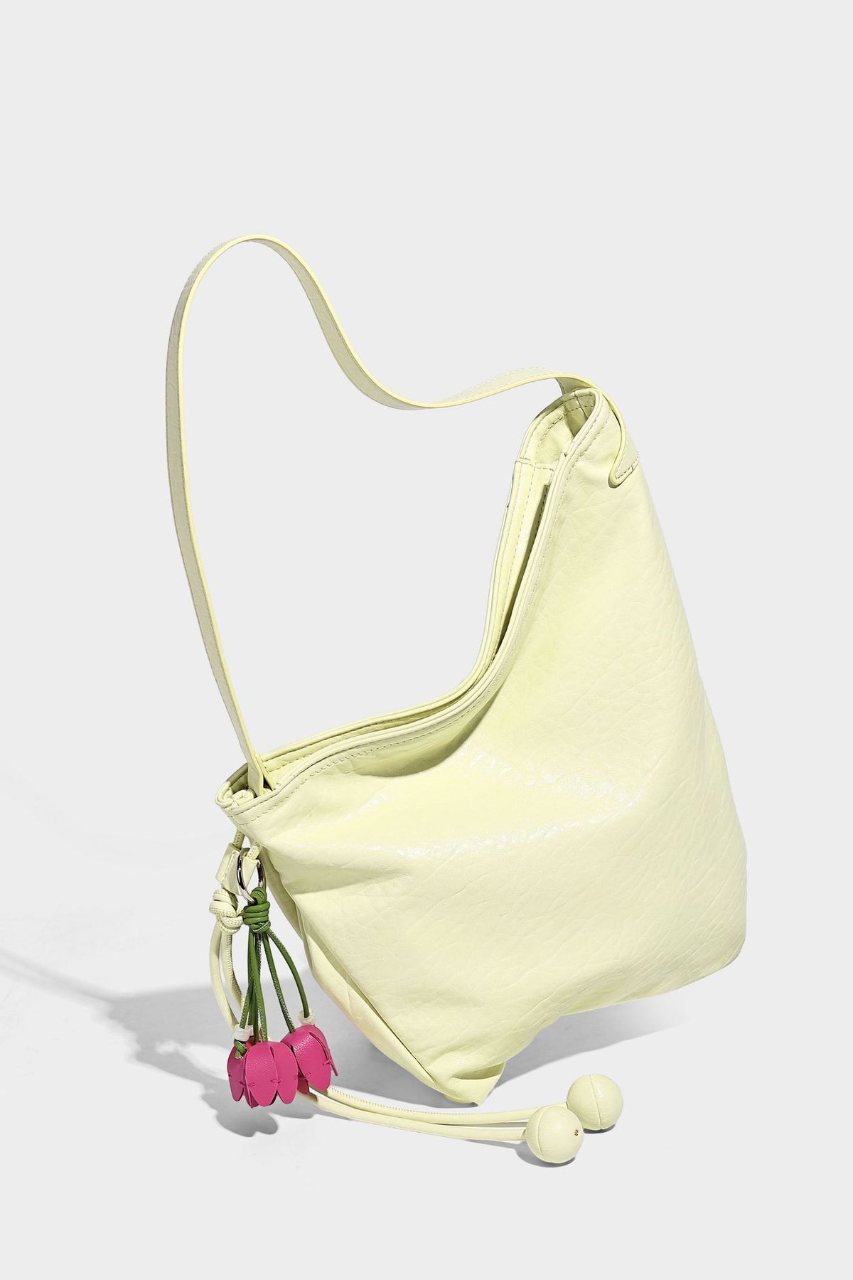 Slouchy hobo shoulder bag in pale yellow with slim strap, drawstring bead closure, and pink tulip floral charm, detail view