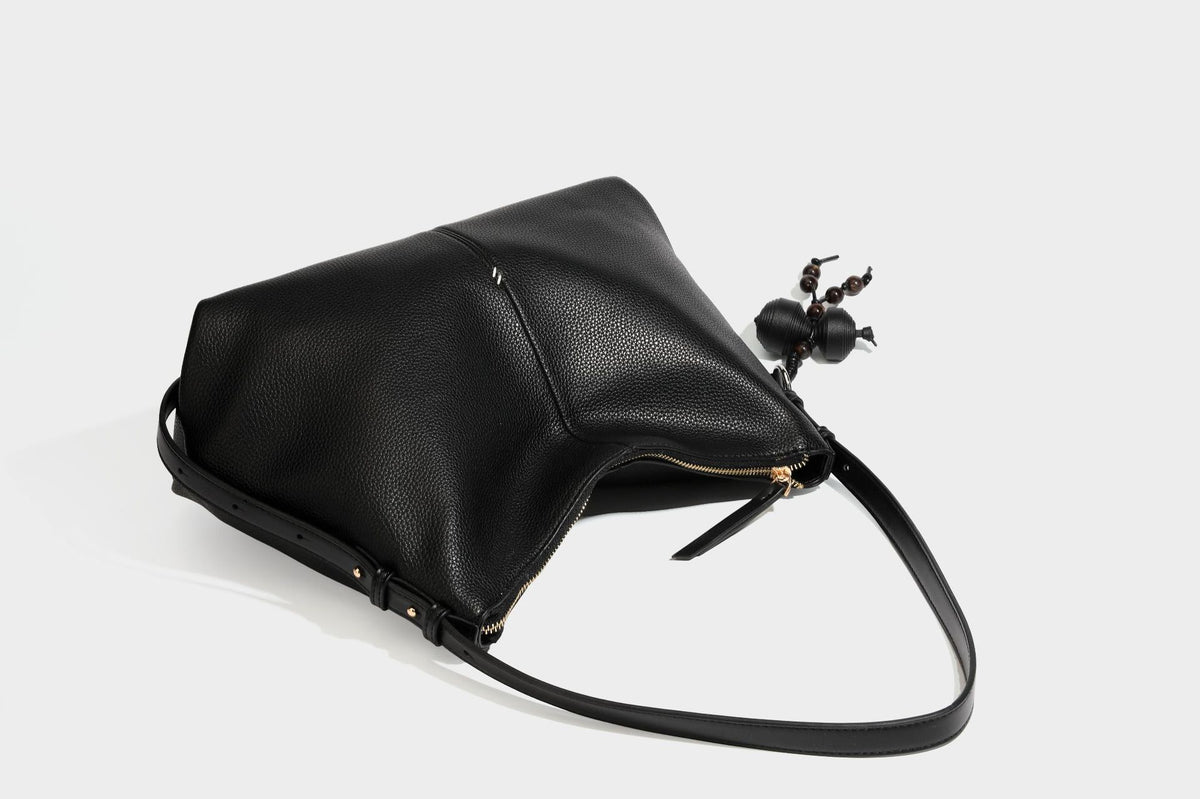 Slouchy hobo shoulder bag with pebbled leather-look finish, zip-top closure, gold-tone hardware, and hanging bead charm