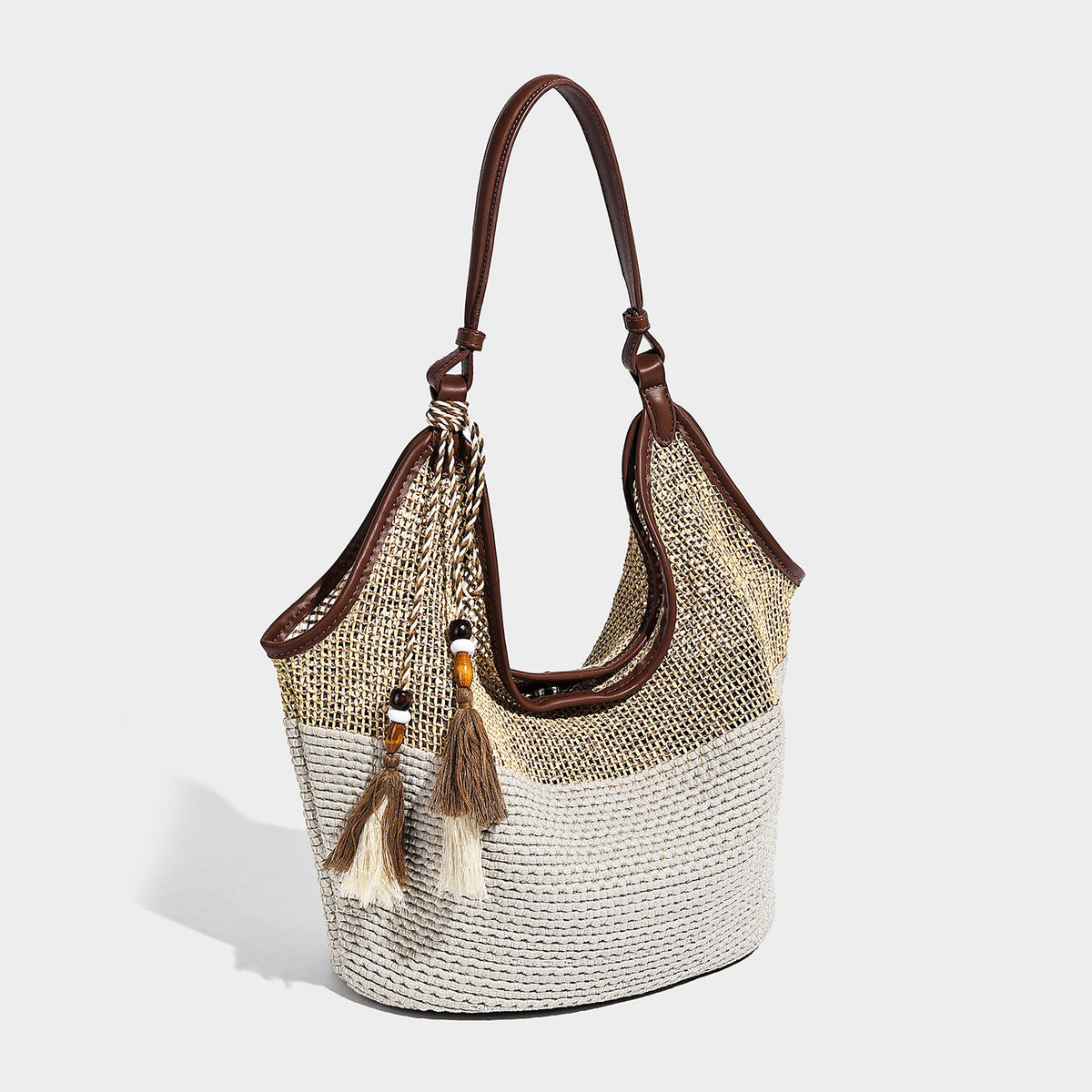 Two-tone beige and cream woven straw hobo shoulder bag with brown leather-look trim, long shoulder strap, and tassel-bead