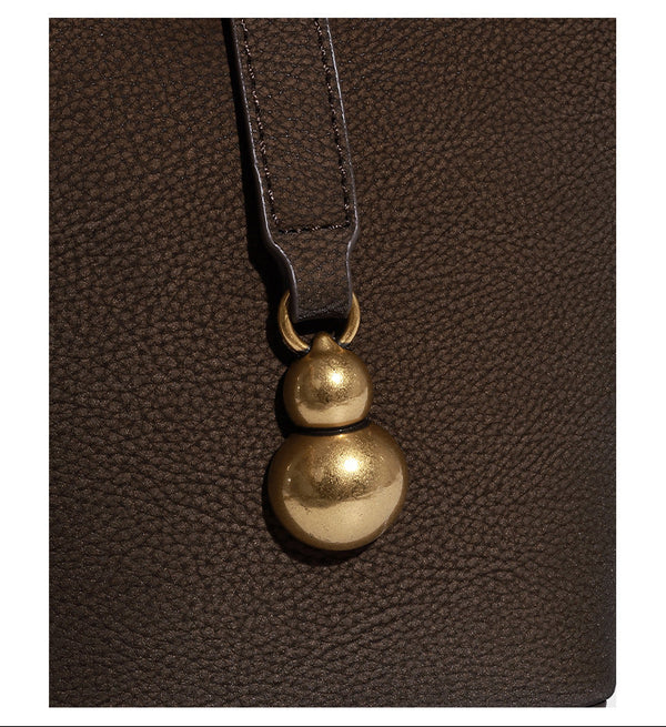 Kleine matte Beuteltasche mit genarbter Oberfläche, antikgoldfarbenen Ringbeschlägen, Perlen- und Quastenanhänger, kurzen Tragegriffen oben und