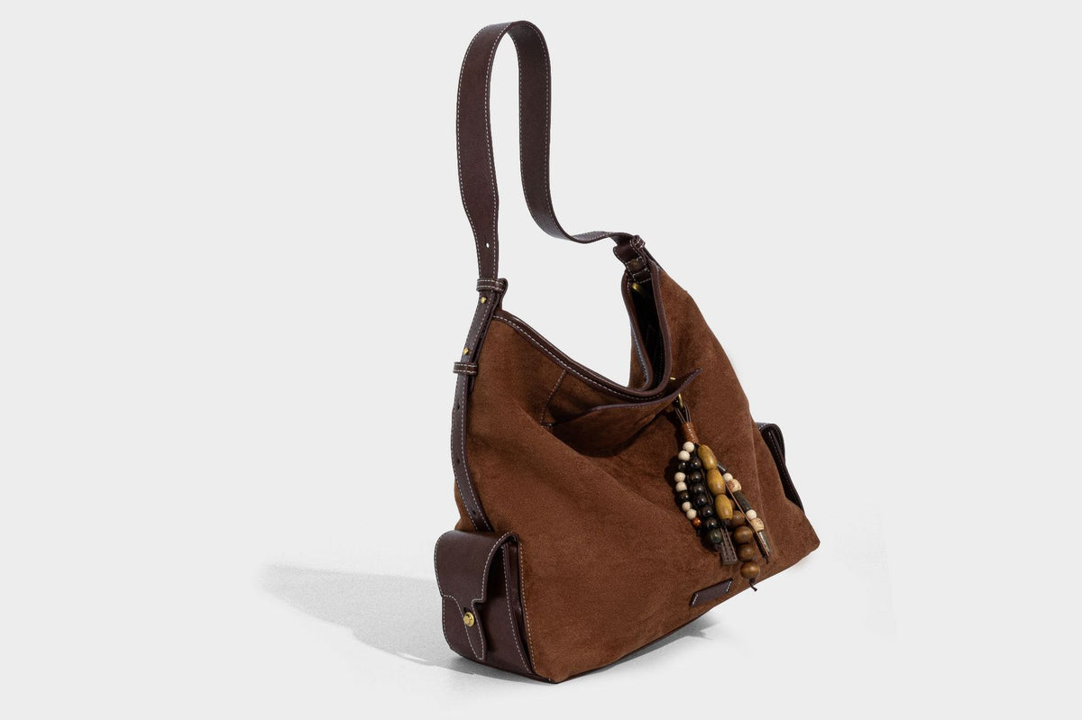 Lässig fallende Hobo-Schultertasche in Khaki aus mattem Material in Wildlederoptik mit dunkelbraunem Besatz in Lederoptik, Quastenanhänger mit Perlen und seitlicher Klappe, Detailansicht