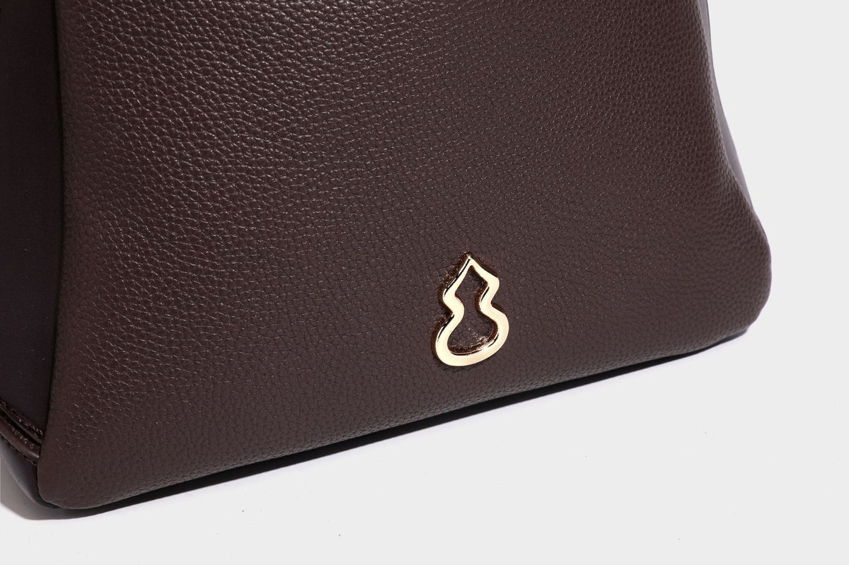 Structured pebbled leather-look shoulder bag with flap top, gold-tone emblem hardware, dual top handles, and detachable