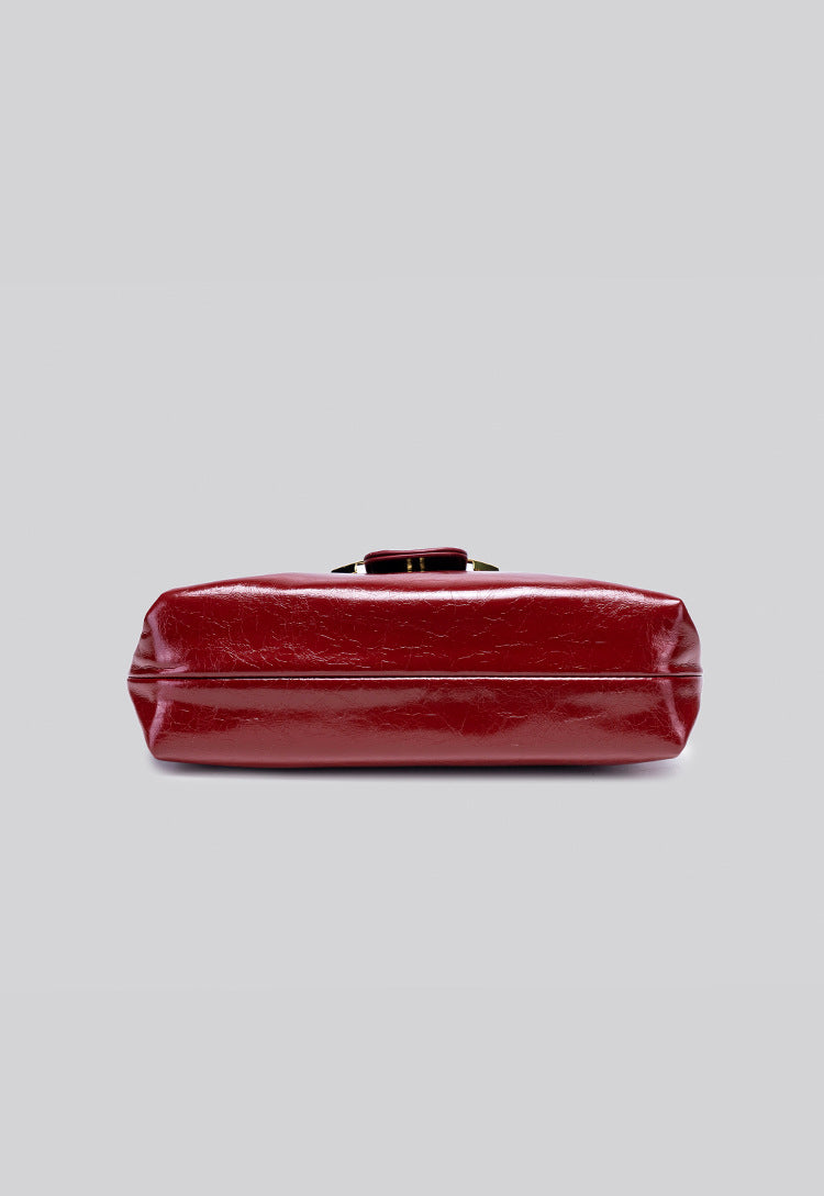 Glossy burgundy leather-look shoulder bag with curved gold-tone bar front closure, crinkled oil-wax texture, and adjustable