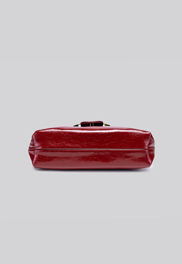 Glossy burgundy leather-look shoulder bag with curved gold-tone bar front closure, crinkled oil-wax texture, and adjustable