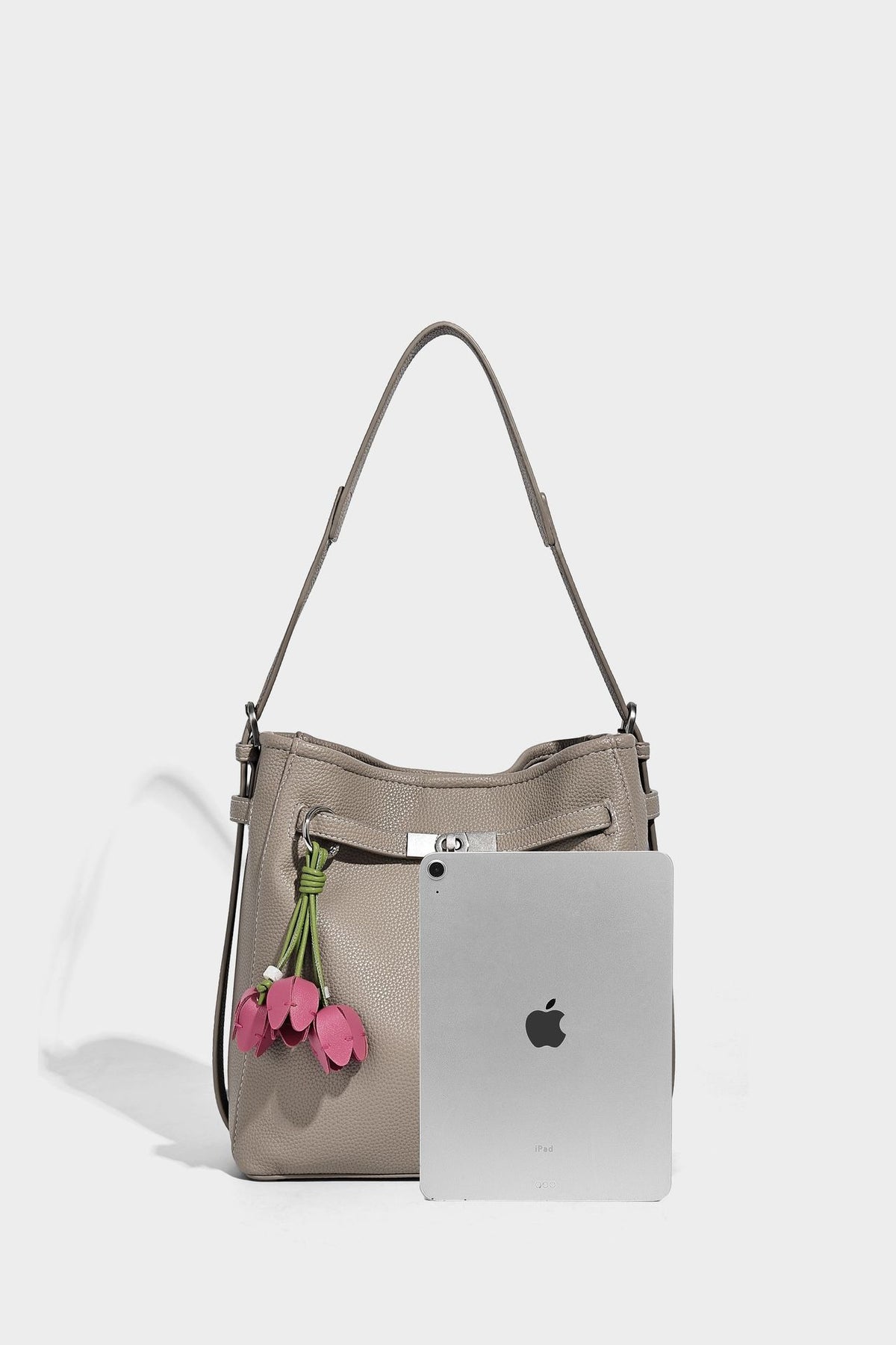 Soft-structured pebbled bucket shoulder bag with front turn-lock strap detail, adjustable strap, and hanging floral tassel