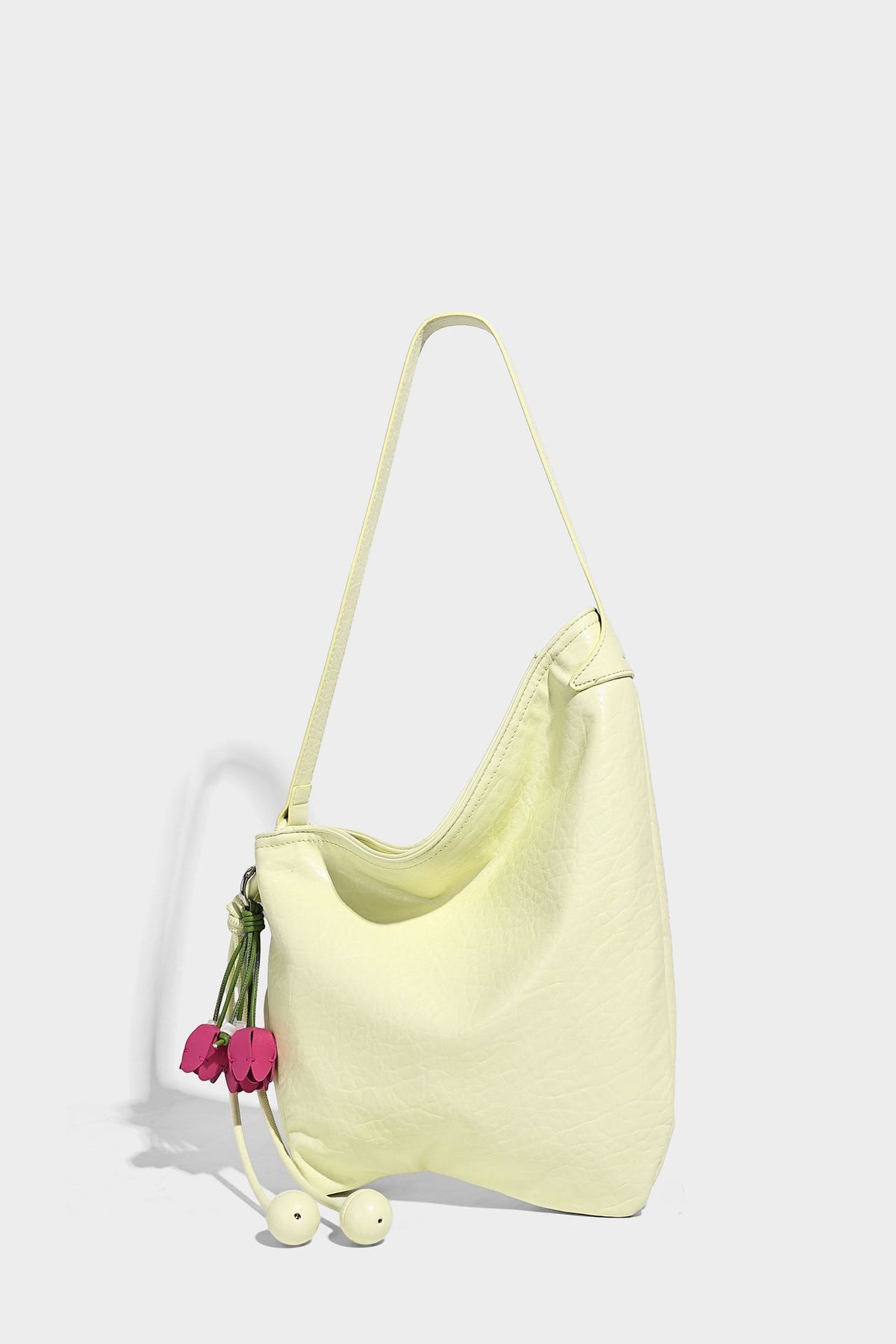 Slouchy hobo shoulder bag in pale yellow with slim strap, drawstring bead closure, and pink tulip floral charm, detail view