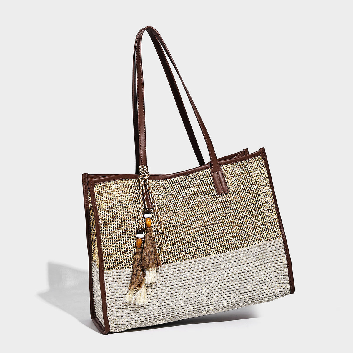 Two-tone woven straw tote bag with leather-look brown trim, long shoulder straps, and knotted tassel charm, detail view 2