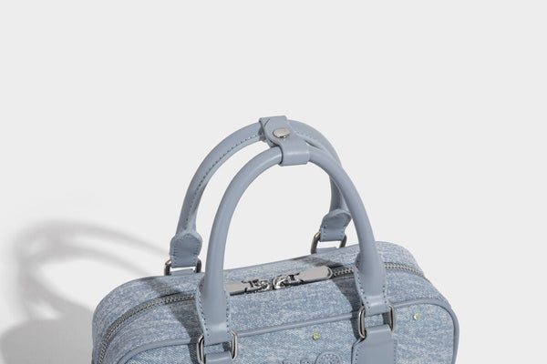 Small light blue denim-look barrel bag with white floral bead embroidery, dual top handles, and detachable shoulder strap