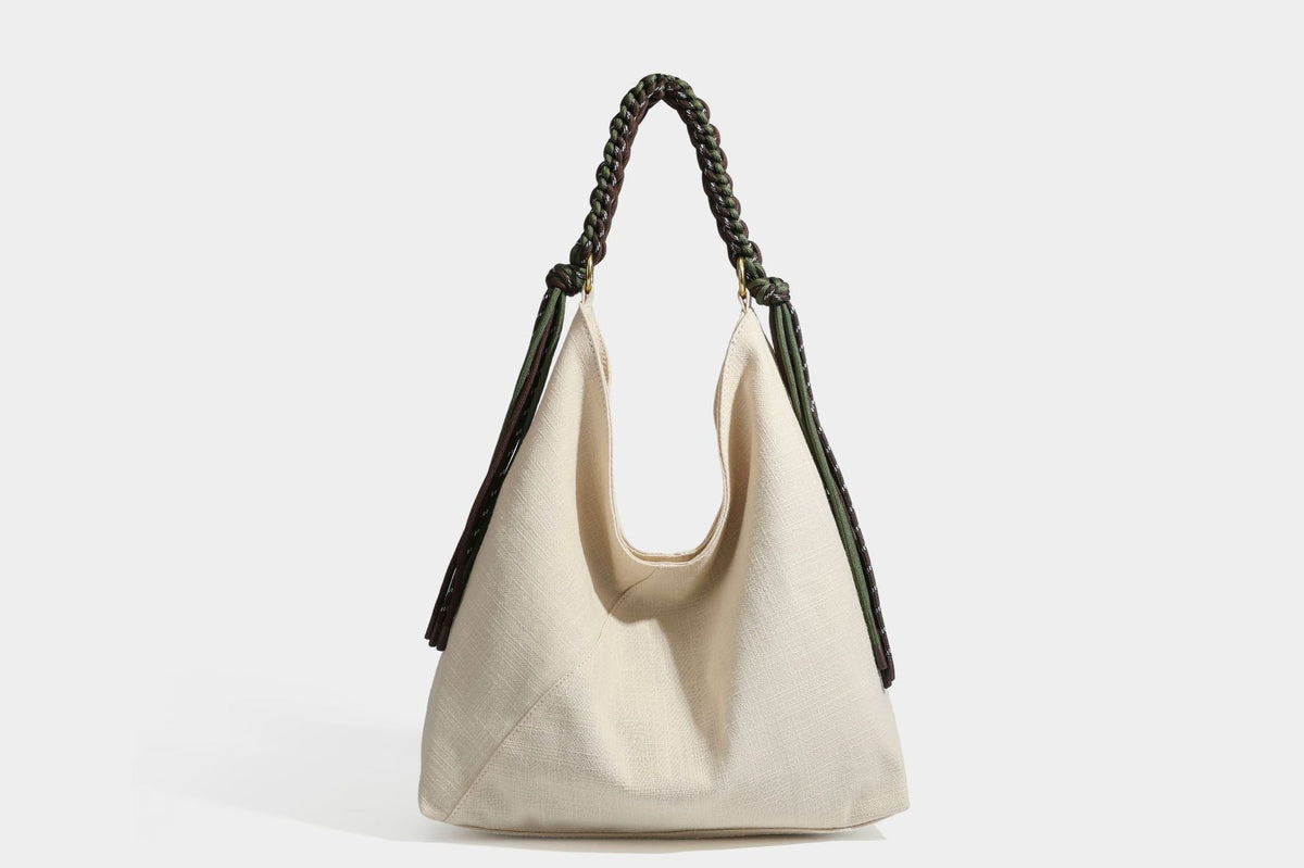 Soft slouchy cream canvas shoulder tote with braided brown and green cord handle, gold-tone ring hardware, and tassel trim