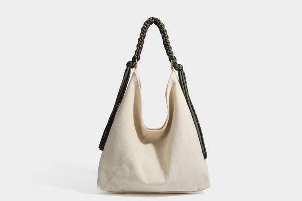 Soft slouchy cream canvas shoulder tote with braided brown and green cord handle, gold-tone ring hardware, and tassel trim