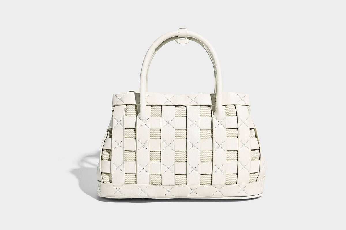 Small structured woven satchel tote with rounded top handles, silver-tone ring hardware, and bead tassel charm, detail view