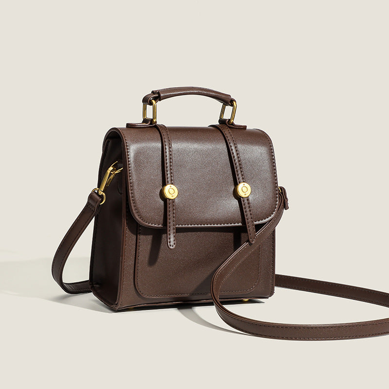 Structured mini satchel backpack with smooth leather-look finish, front flap pocket, gold-tone stud closures, and top handle