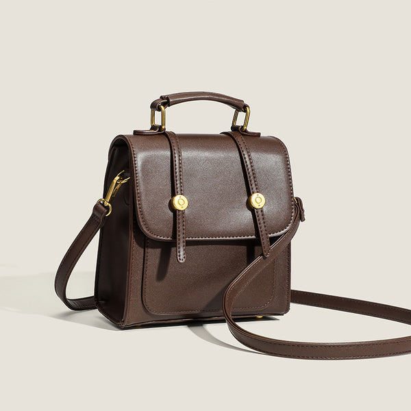 Structured mini satchel backpack with smooth leather-look finish, front flap pocket, gold-tone stud closures, and top handle
