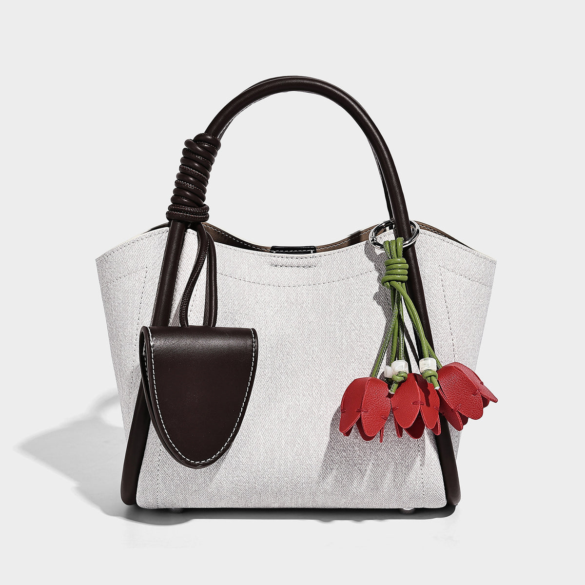 Light blue denim trapezoid tote bag with black leather-look trim, knotted top handles, detachable crossbody strap, front