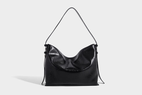 Large slouchy hobo shoulder bag in glossy crinkle leather-look finish with gold-tone emblem hardware and adjustable strap