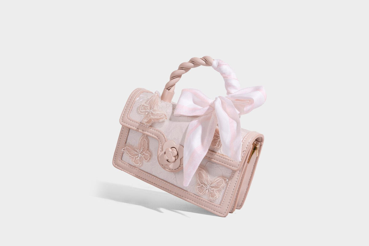 Small structured white flap bag with butterfly embroidery, flower-shaped turn-lock clasp, braided top handle with scarf bow