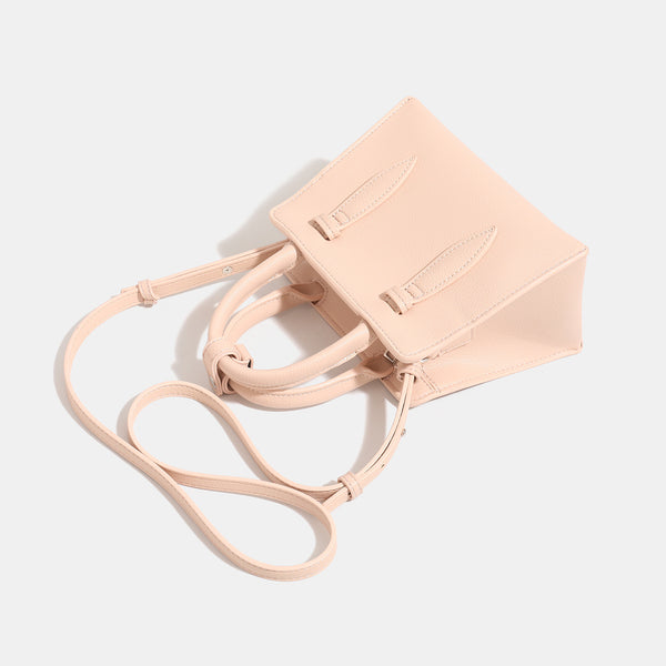 Small structured trapezoid top-handle bag in pebbled matte finish with decorative strap tabs, twin knotted handles, and