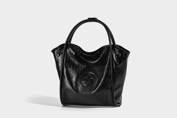 Glossy leather-look structured tote bag with rounded top handles, detachable shoulder strap, embossed front emblem, and side