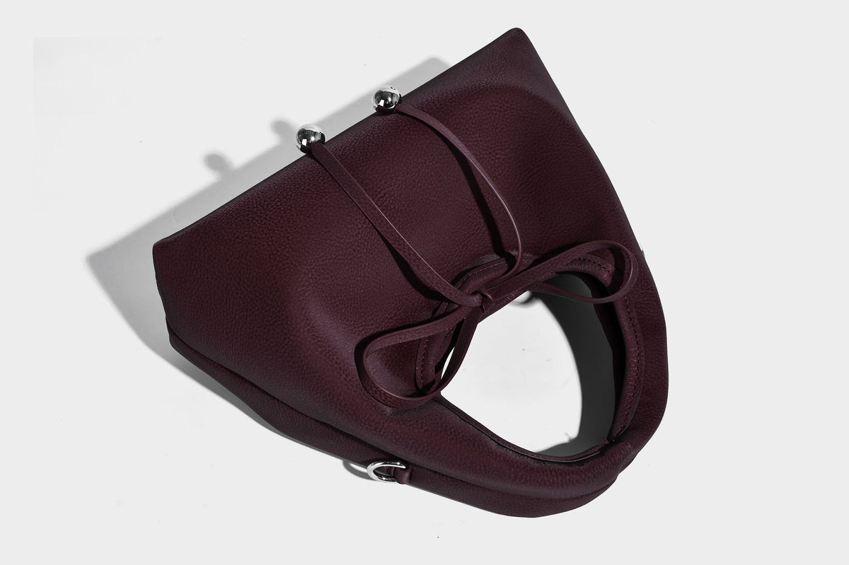 Pebbled matte trapezoid top-handle bag with drawstring bow closure, bead-tipped cords, silver-tone hardware, and detachable