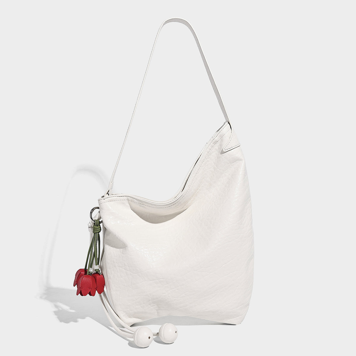 Slouchy hobo shoulder bag in pale yellow with slim strap, drawstring bead closure, and pink tulip floral charm, detail view