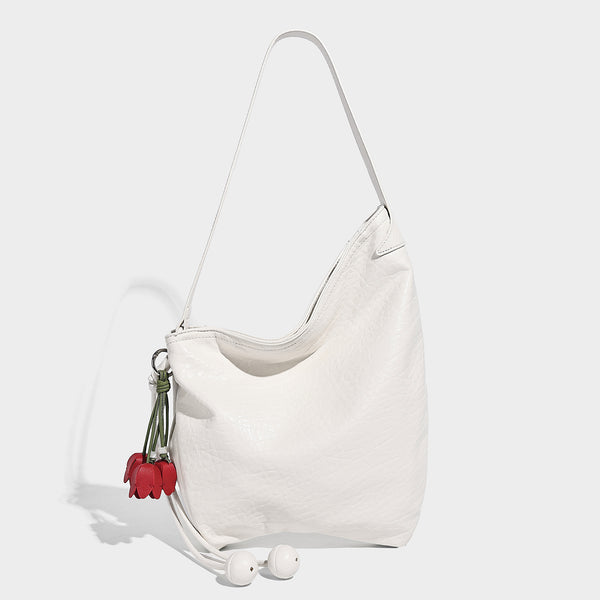 Slouchy hobo shoulder bag in pale yellow with slim strap, drawstring bead closure, and pink tulip floral charm, detail view