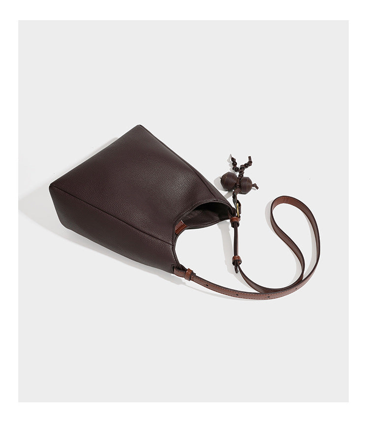 Hobo-Schultertasche in dunklem Espresso mit genarbter Oberfläche, warmen cognacfarbenen Details, verstellbarem schmalem Riemen, goldfarbenen Ringbeschlägen und geknotetem