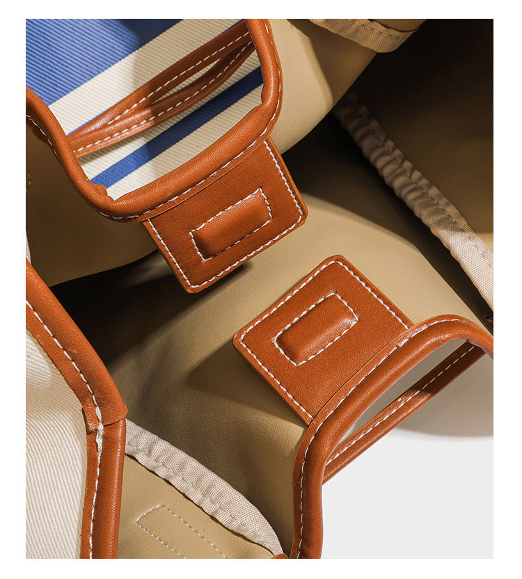 Large cream and navy striped canvas bucket tote bag with tan leather-look trim, drawstring closure, and double shoulder