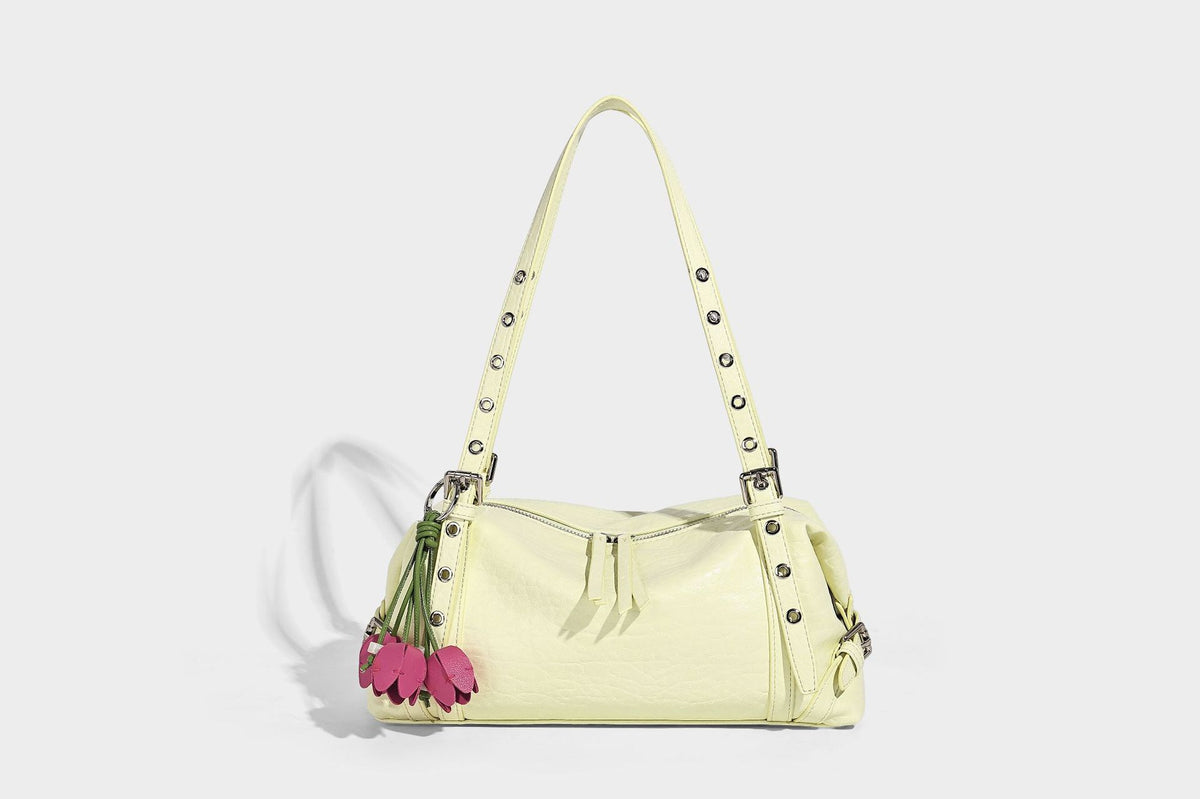 Pale yellow leather-look barrel bag with silver grommet-studded shoulder straps, top zip closure, and pink tulip floral
