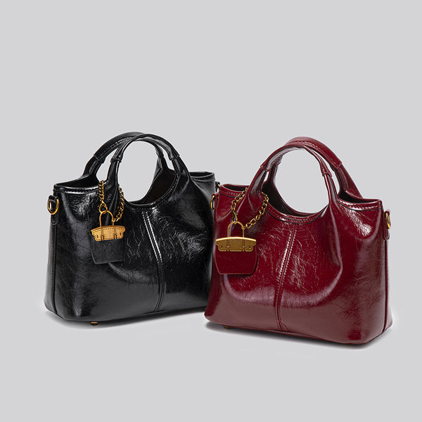 Structured crinkle-gloss top-handle satchel in deep burgundy with antique gold lock charm and detachable shoulder strap