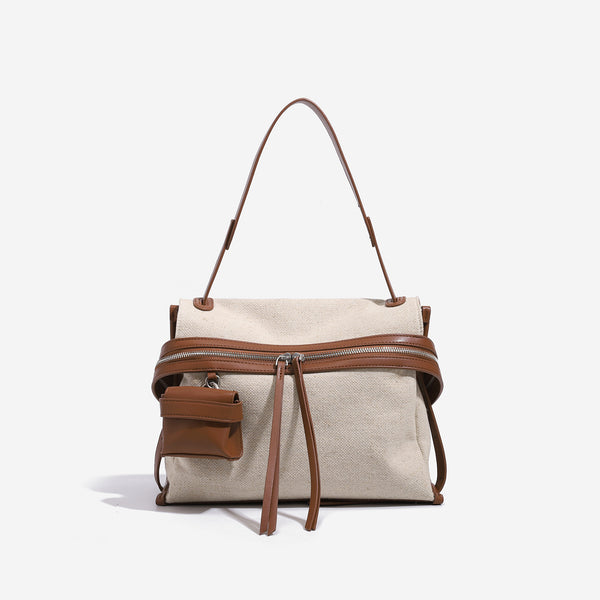 Cream canvas zip-top shoulder bag with cognac leather-look trim, dual zipper, attached mini pouch, and tassel strap ties