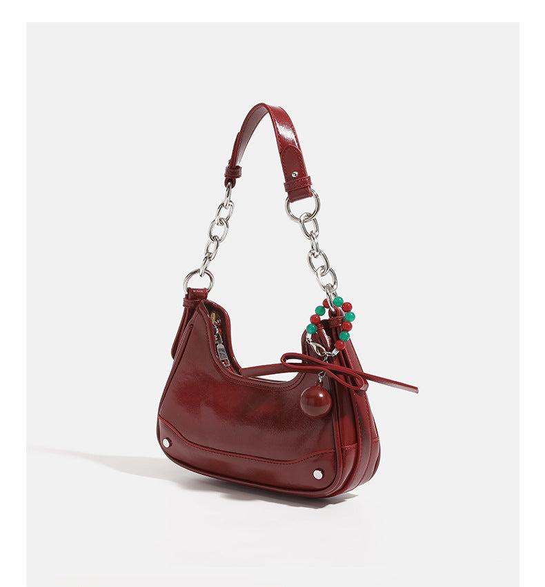 Compact crescent hobo shoulder bag in glossy burgundy leather-look finish with silver chain strap, red and green bead tassel