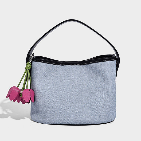Small denim-look bucket bag with black leather-look trim, pink tulip flower charm, and adjustable crossbody strap, detail
