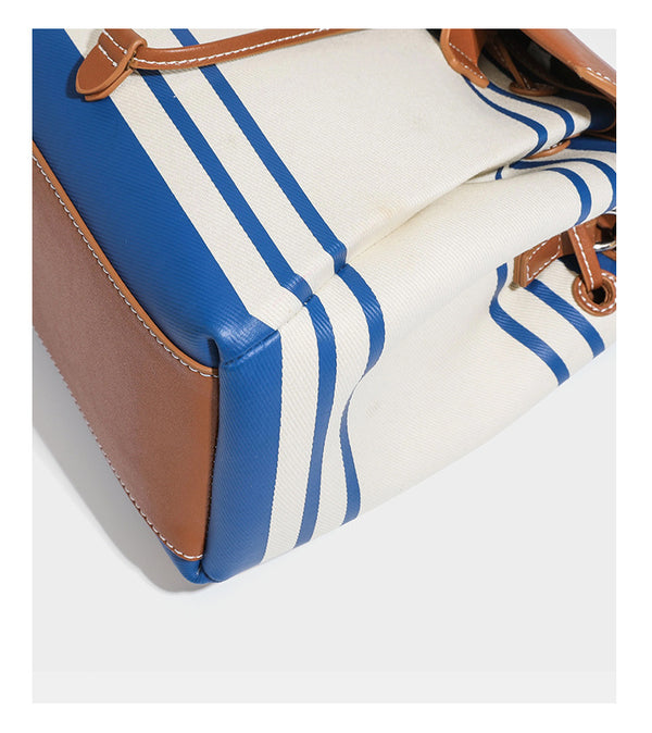Cream canvas bucket bag with blue horizontal stripes, tan leather-look flap and trim, drawstring closure, silver-tone, detail