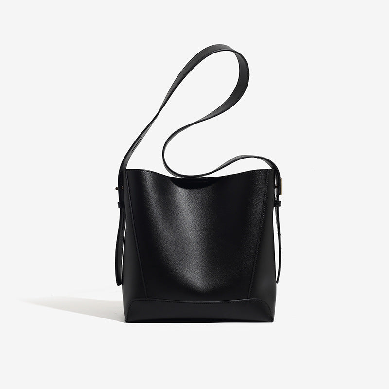 Structured smooth leather-look bucket shoulder bag with long adjustable strap and gold-tone buckle hardware in brown, detail