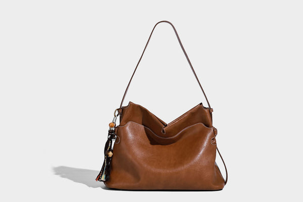 Large slouchy leather-look hobo tote bag with open top, adjustable shoulder strap, and colorful tassel bead charm, detail