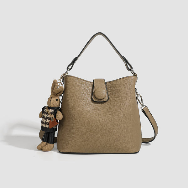 Structured taupe pebbled-texture bucket bag with top handle, silver ring hardware, tab-and-button closure, and knit bunny