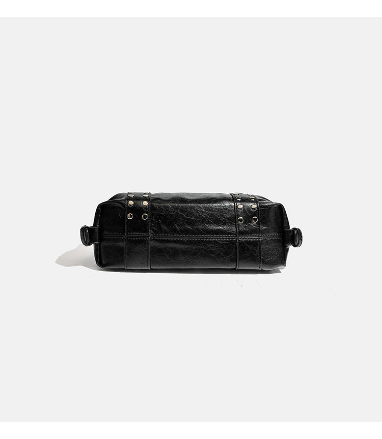 Compact black glossy leather-look satchel bag with silver-tone rivets, buckle hardware, and dual padded top handles, detail
