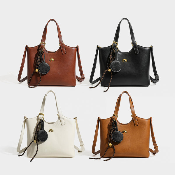 Structured smooth leather-look tote bag with long shoulder strap, gold-tone hardware, and hanging tassel-coin charm, detail