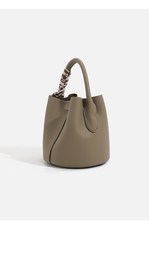 Pebbled leather-look bucket bag with checkered scarf-wrapped top handle, flap tab closure, gold-tone hardware, and matching